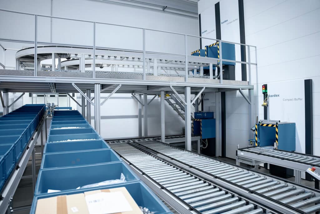 Automatisierte Förderstrecke mit Robotunits Komponenten bei der Intralogistiklösung von Kardex für Böllhoff – verbunden mit vertikalen Pufferliften im Lagerbereich