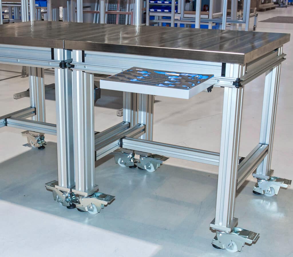 Robuster Schwerlast-Arbeitstisch von Robotunits mit massiver Edelstahl-Arbeitsplatte für besonders anspruchsvolle Anwendungen. Stabiler Rahmen aus Aluminiumprofilen, ausgestattet mit Schwerlastrollen und integrierter Werkzeugschublade. Ideal für den Einsatz in Produktionsbereichen mit hohen mechanischen Belastungen.