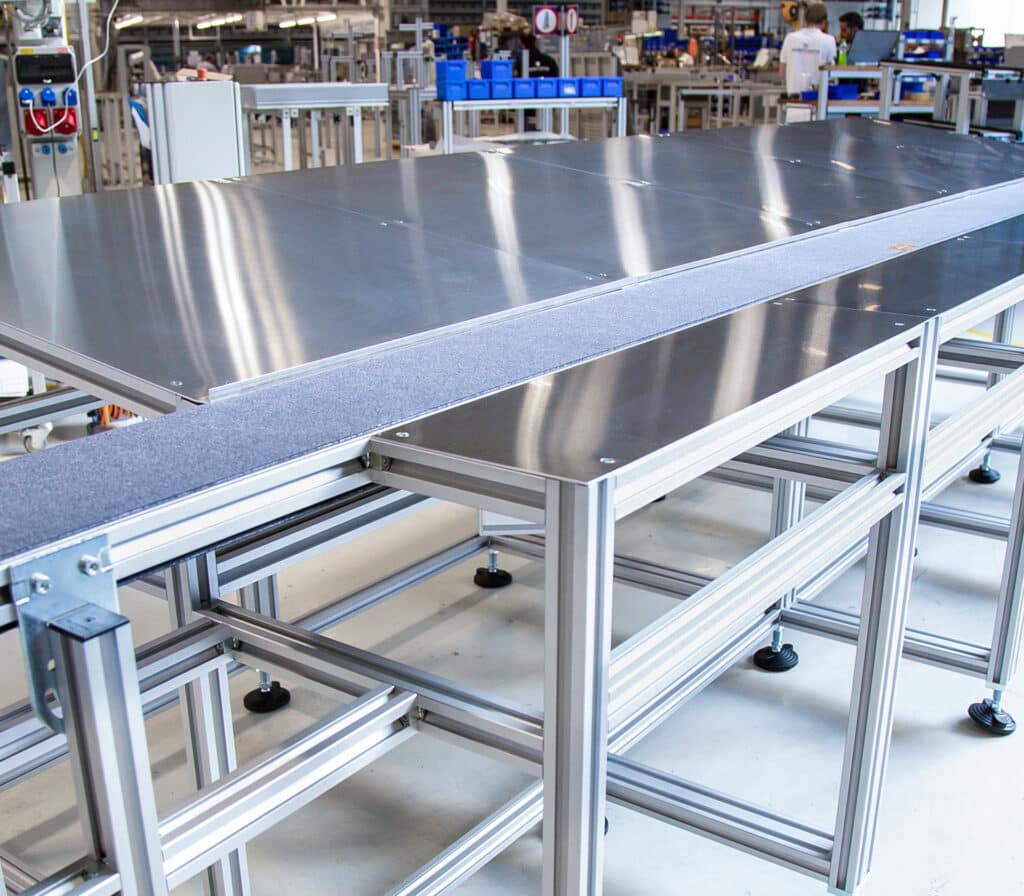 Modularer Robotunits-Arbeitstisch mit integrierter Gurtförderstrecke für den nahtlosen Materialfluss entlang der Edelstahl-Arbeitsflächen. Die stabile Aluminiumprofilkonstruktion ermöglicht eine präzise Ausrichtung und flexible Erweiterung. Ideal für durchgängige Montage- und Fertigungsprozesse mit hoher Effizienz.